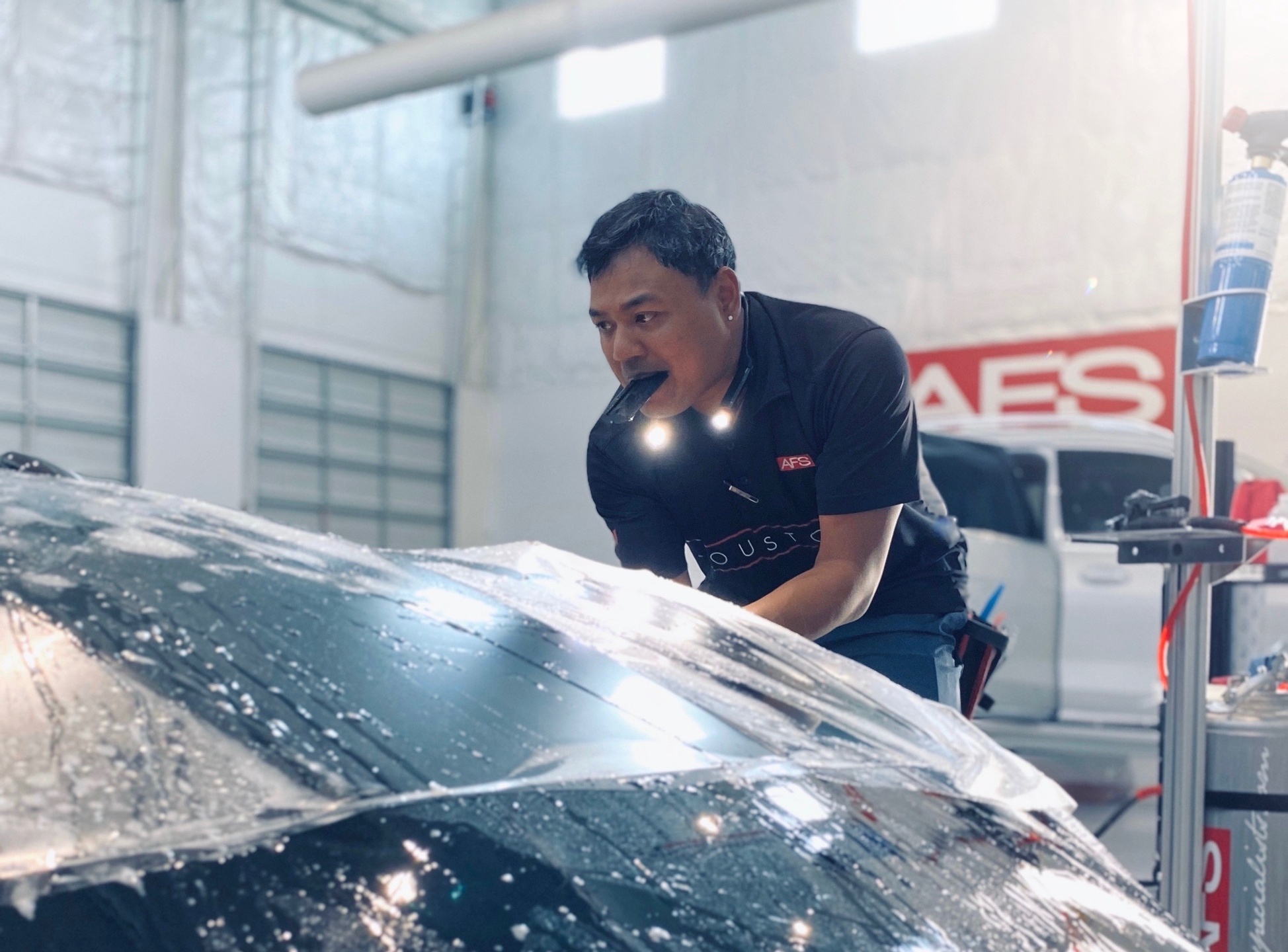 An installer works with paint protection film on a wet car hood.